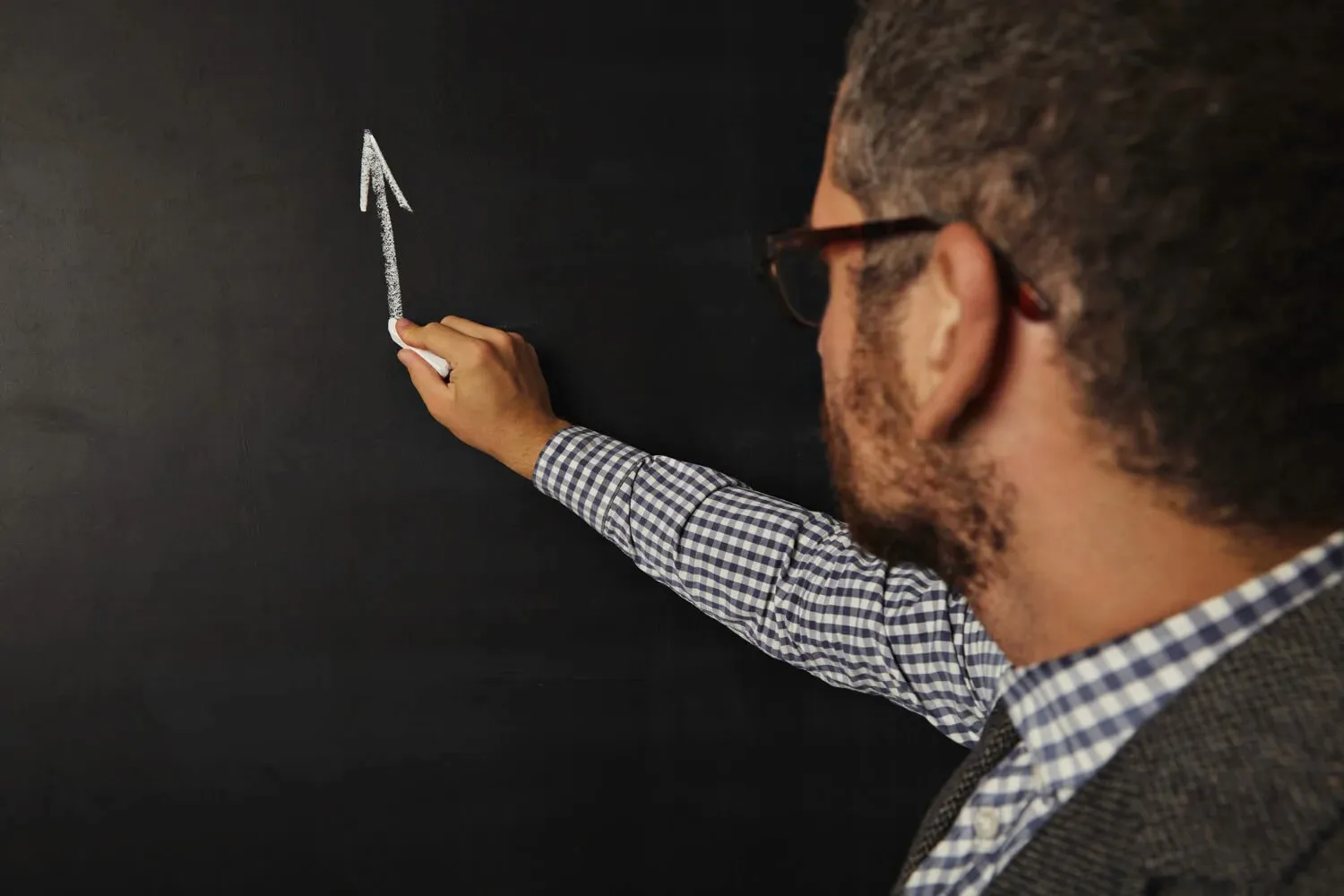A bearded man in glasses drawing an upward growth arrow on a chalkboard.
